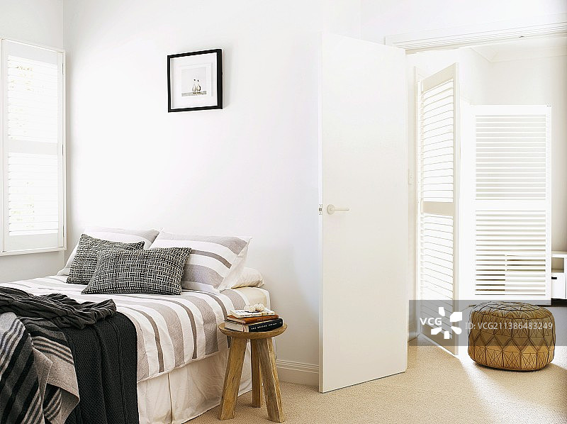 明亮的睡眠区，配有开放式百叶门，窗户下的床和床边凳子上的一堆书图片素材