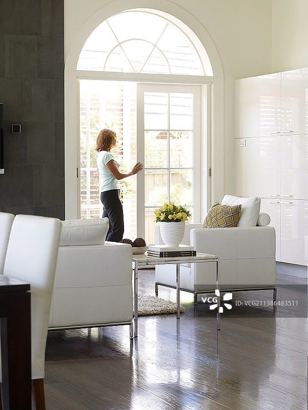 休息区配有立方皮革扶手椅；后面是一位女士，站在拱形法式门前图片素材