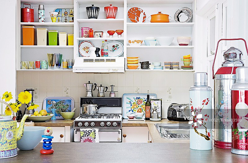 白色厨房搁架上的彩色陶器；前景中工作台面上颜色鲜艳的保温瓶图片素材