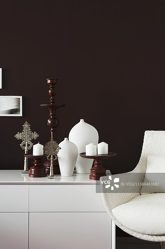 白色光面餐具柜上靠复古扶手椅的木制烛台和蜡烛图片素材