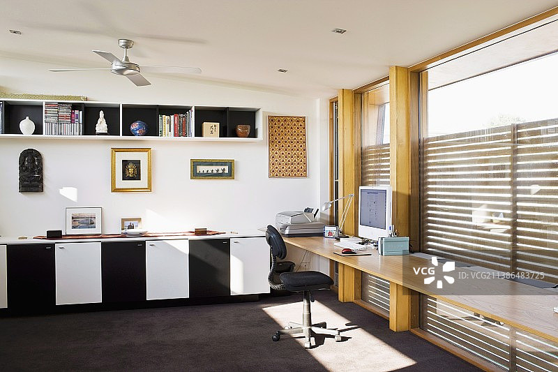 宽敞的家庭办公室，靠墙的书桌，窗户墙；底柜上方有图片和雕塑，黑白门图片素材