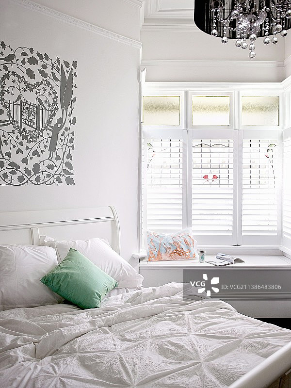 白色双人床，带有绿色靠垫，墙上有浪漫印花；舒适的窗台位于窗户壁龛中图片素材
