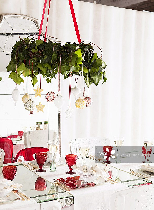 装饰有圣诞球的花环悬挂在摆放着红色复古葡萄酒杯的餐桌上方图片素材