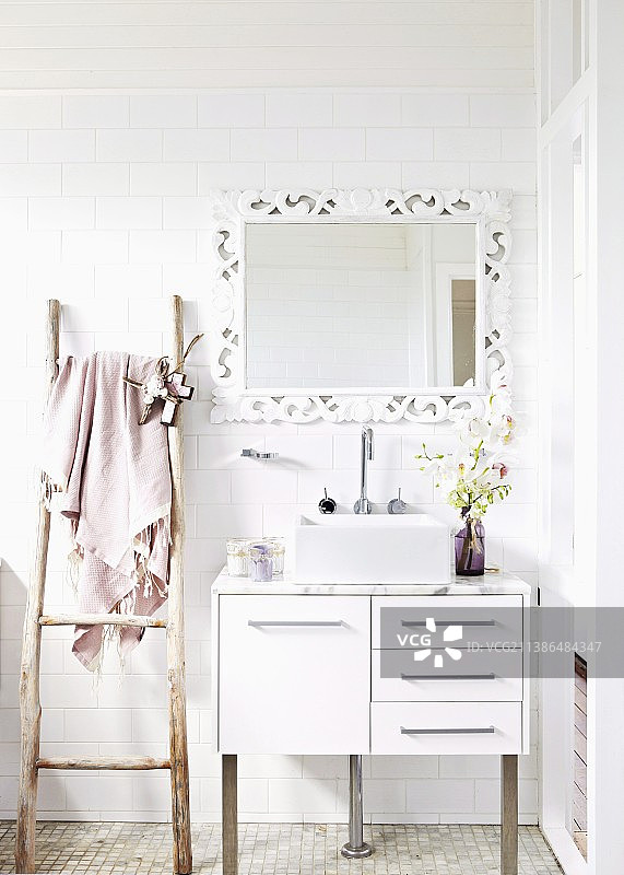 水槽，带有白色瓷砖墙壁的底柜，以及用作毛巾架的质朴木梯旁的镜子图片素材