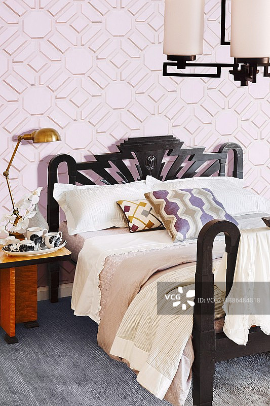 黑色框架双人床，背景是带有图案的粉色墙纸图片素材