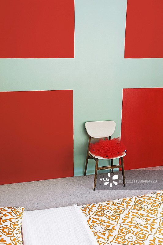 红色织物椅子靠墙，墙面绘有红色和蓝绿色图案，床铺铺有装饰图案床单图片素材