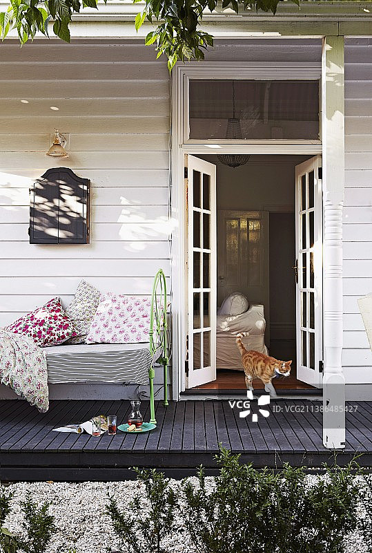 白色木制房屋，猫从法式落地窗走出，舒适的复古沙发床，黑色木制露台图片素材