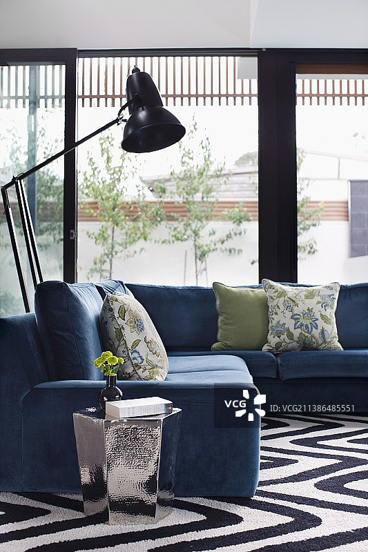 舒适的灰蓝色转角沙发、复古落地灯和玻璃墙前的光亮边桌图片素材