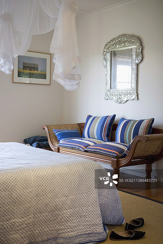 老式条纹软垫脚凳，银框镜子对面是带有优雅床罩的床，上方悬挂着通风的织物天篷图片素材