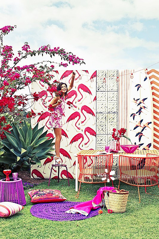 红色和紫色调的火烈鸟印花图案、户外家具和配饰；女人站在凳子上挂着彩灯图片素材