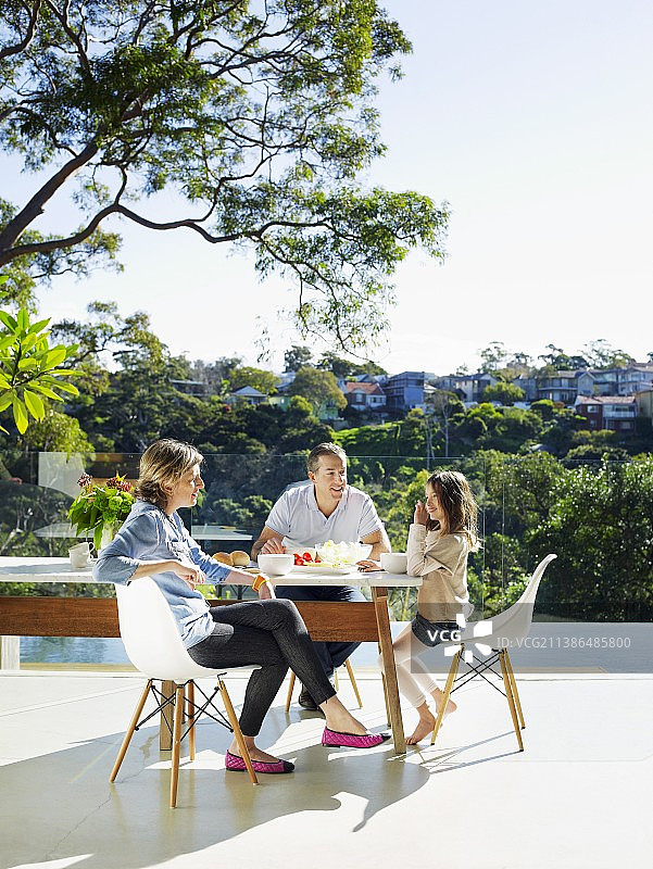 一家人坐在阳光明媚的露台上，设计师桌旁的经典椅子上图片素材