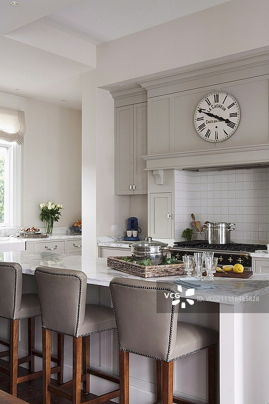 典雅的开放式乡村别墅厨房，配有早餐吧台和皮革吧台凳以及复古挂钟图片素材