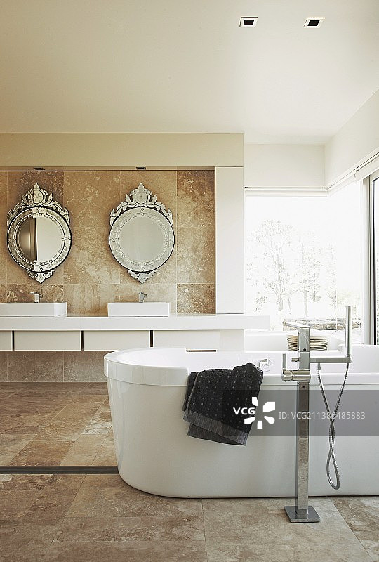 大理石瓷砖浴室内的独立式浴缸；圆形、华丽的古董风格镜子下的盥洗台图片素材