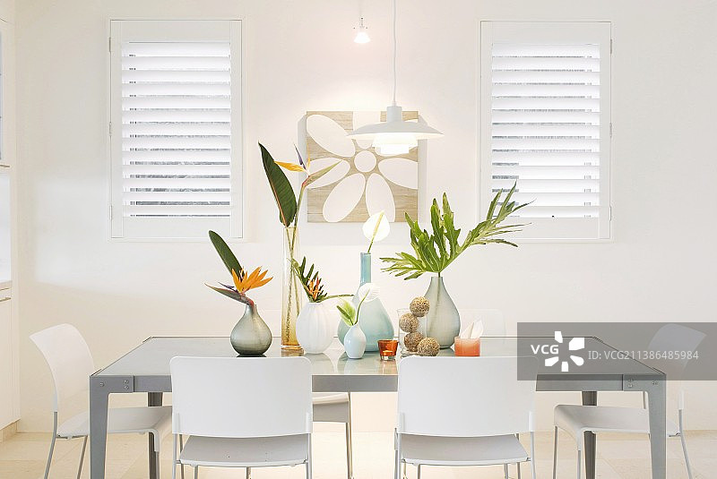 光线明亮的用餐区，摆放着白色椅子和各种天堂鸟鲜花及棕榈叶图片素材