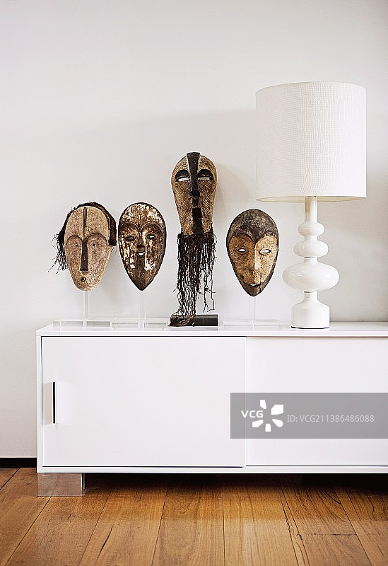 透明塑料支架上的非洲面具，旁边是设计师餐具柜上的白色台灯图片素材