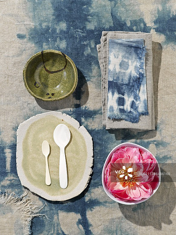 蜡染桌布上碗中鲜花旁边的白色勺子和手工板俯视图图片素材