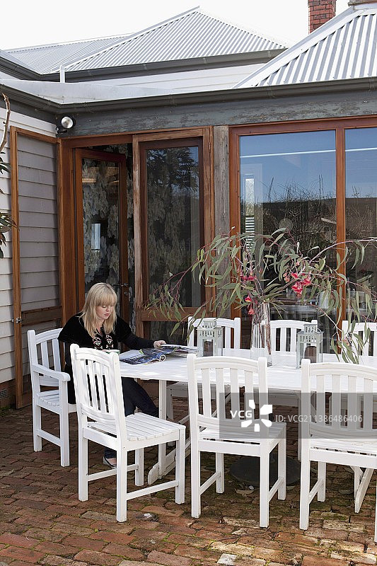 在露台上的女人；木屋外的砖地上有白色户外椅子和桌子，配有落地露台窗户图片素材