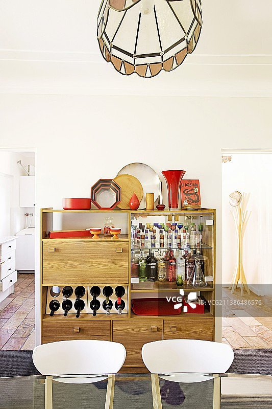 小型家庭酒吧前的椅子靠背与红色装饰品；透过敞开的门可以看到厨房台面和衣帽架图片素材