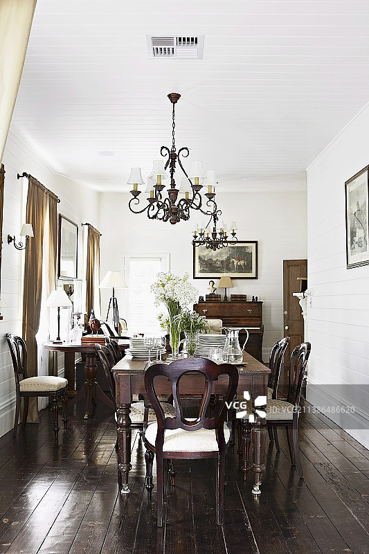 传统优雅的餐厅，配有餐桌、古董椅、锻铁吊灯和深色木地板图片素材