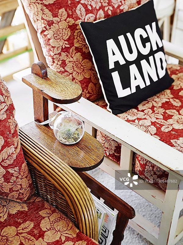 印有“奥克兰”标语的黑白靠垫，置于花卉扶手椅旁边的杂志架上图片素材
