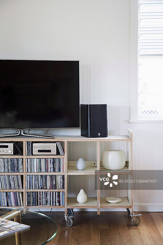 电视、扬声器、CD和花瓶，放置在带脚轮的开放式复古搁架上图片素材