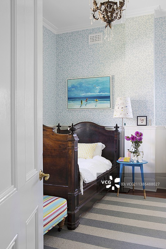 透过敞开的房门看到的古董雪橇床和蓝色床头柜，背景是木镶板和壁纸墙图片素材