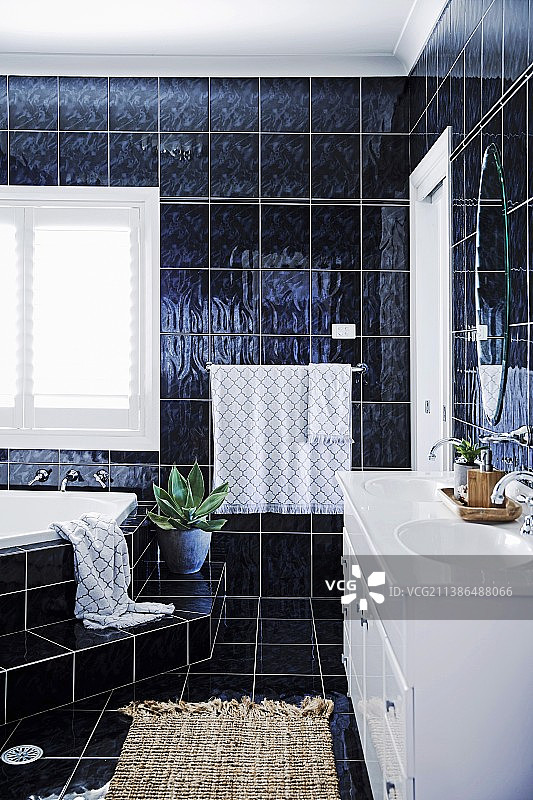 带深色墙面和地砖、带台阶的转角浴缸和白色梳妆台的浴室图片素材