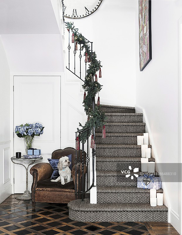装饰过的圣诞楼梯，台阶上有白色蜡烛，舒适的皮革扶手椅旁有一只小狗图片素材