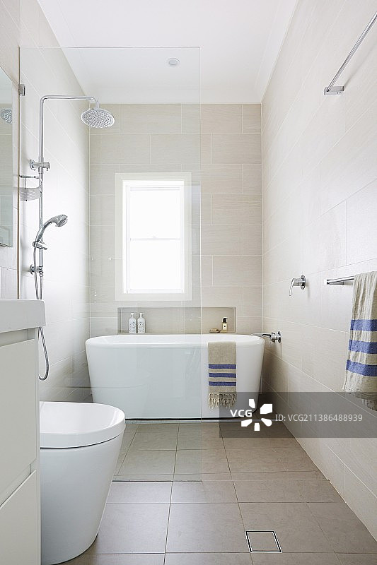 浴室配有玻璃淋浴隔断和窗前的独立式白色浴缸图片素材