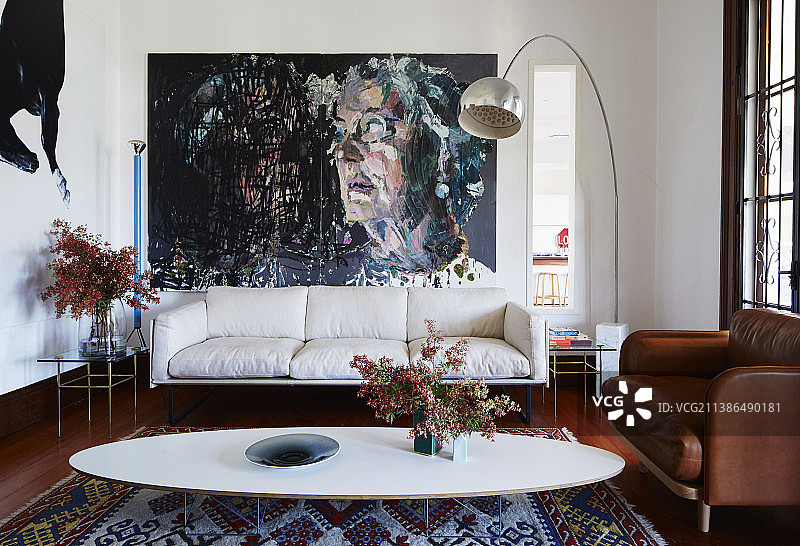 客厅里的经典椭圆形咖啡桌、沙发、弧形落地灯和大画幅绘画图片素材