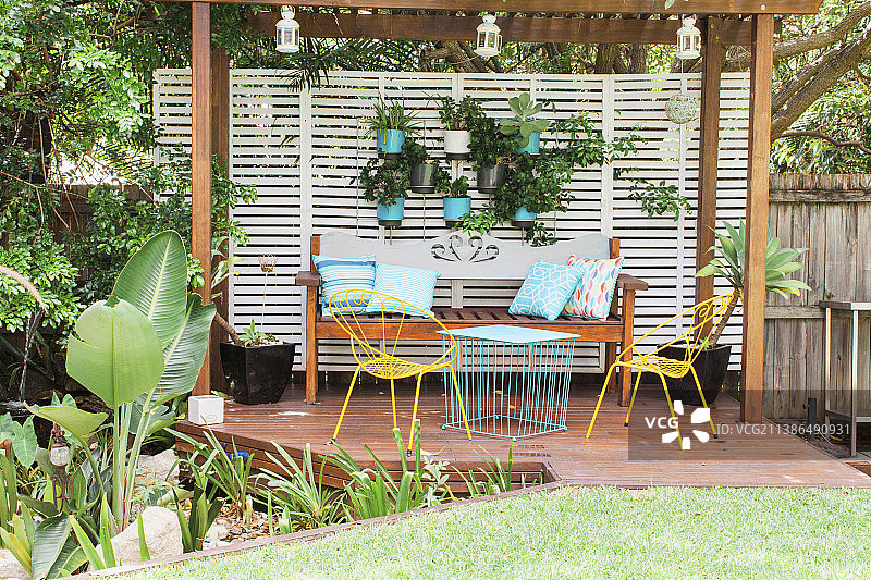 带有木制长凳、金属椅子、桌子和悬挂植物盆的凉棚图片素材