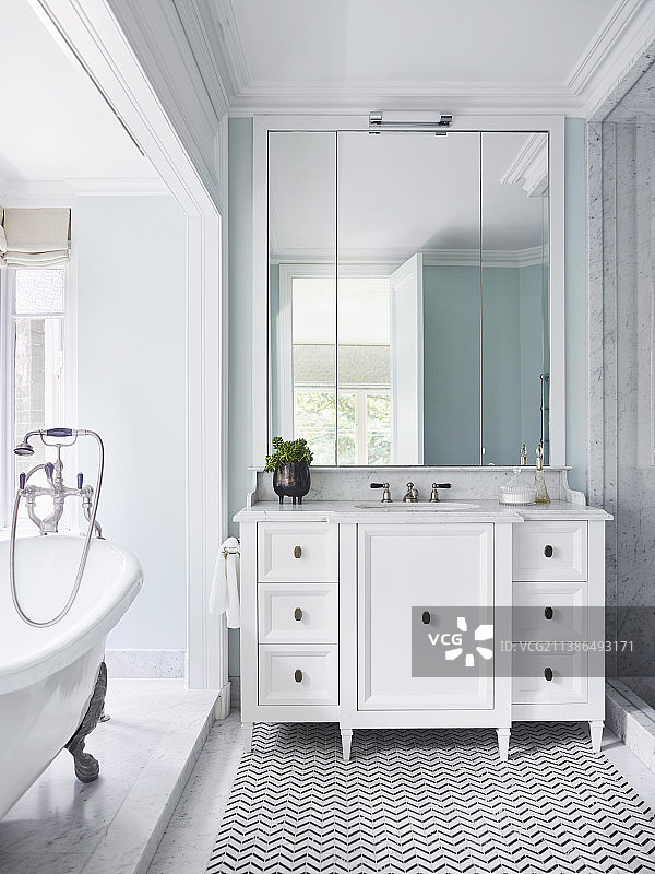 优雅浴室中白色梳妆台和独立式浴缸上的墙壁镜子图片素材