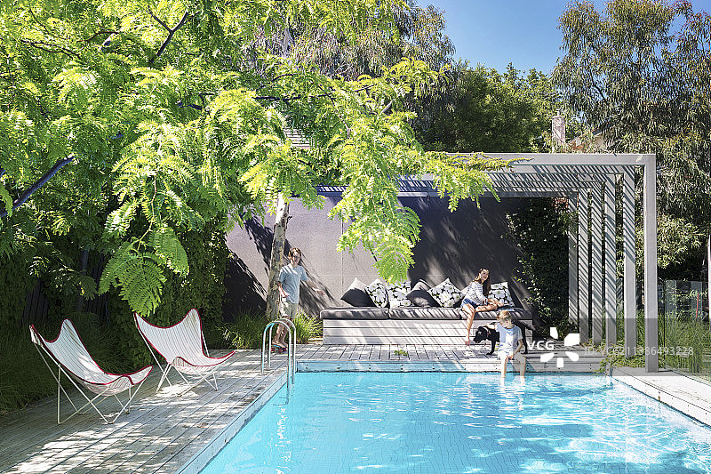 在花园游泳池旁的一家三口和宠物狗图片素材