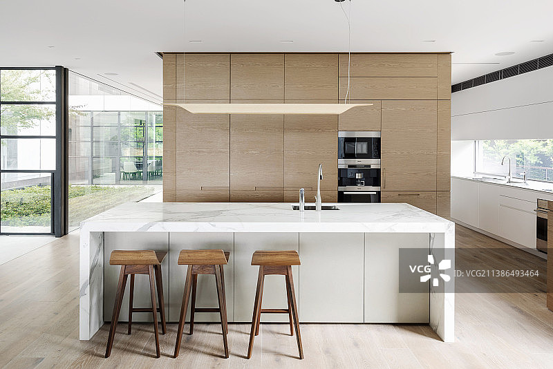 设计师厨房，中央大理石台和吧台椅，开放式客厅配有玻璃幕墙图片素材