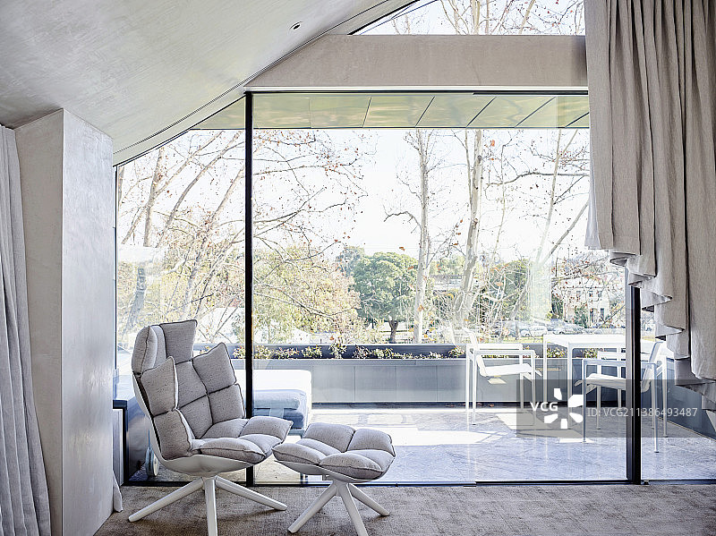 玻璃幕墙前的设计师扶手椅和脚凳图片素材