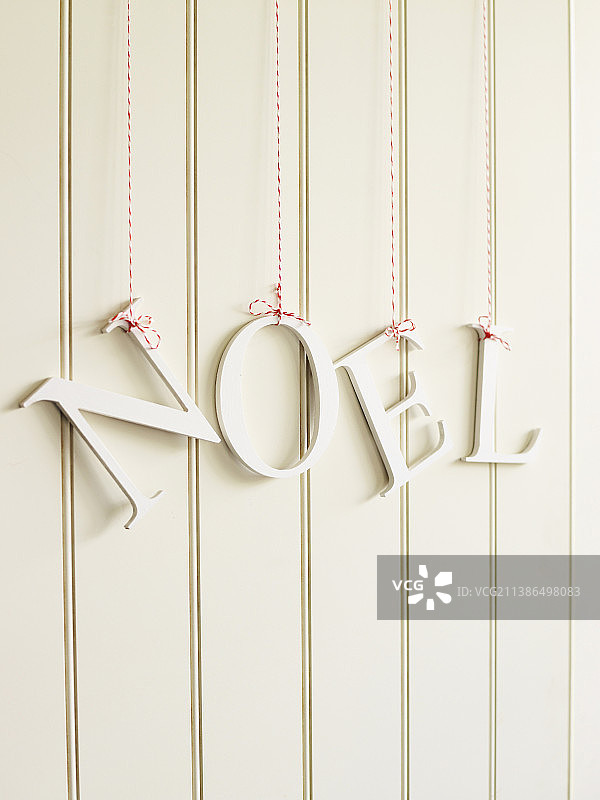 装饰字母“NOEL”悬挂在白色木墙上的红白绳子上图片素材