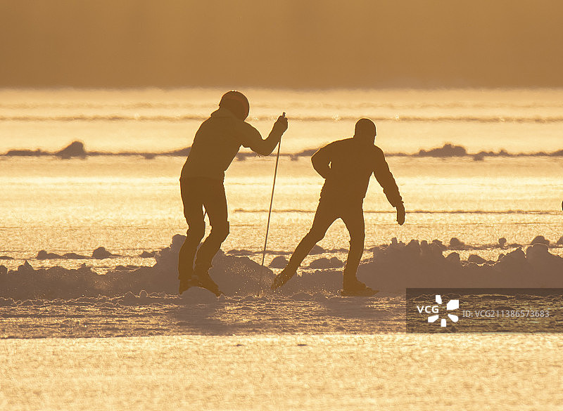 日落时分，在冬季的天空下，两个人穿着雪鞋的轮廓图片素材