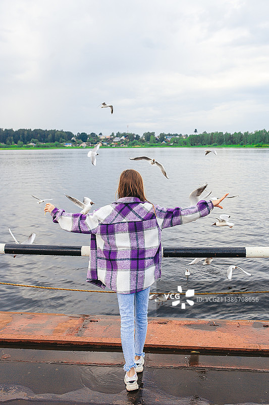 年轻女孩看着飞过湖面的鸟的背影图片素材