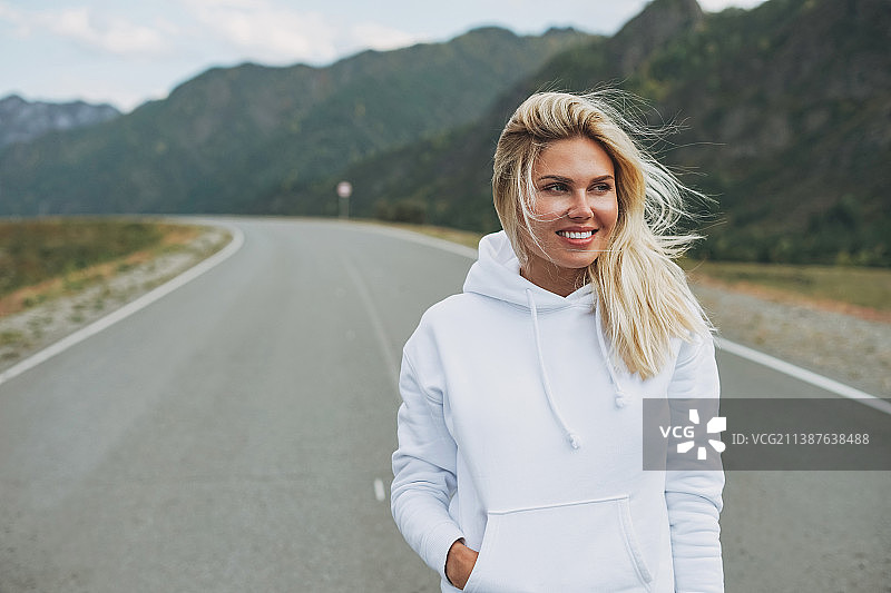 美丽微笑的金发年轻女子旅行者在路上穿白色卫衣，旅行到山区，阿尔泰图片素材
