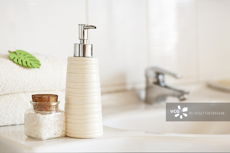 陶瓷皂、洗发水瓶、浴盐玻璃瓶和白色棉毛巾图片素材
