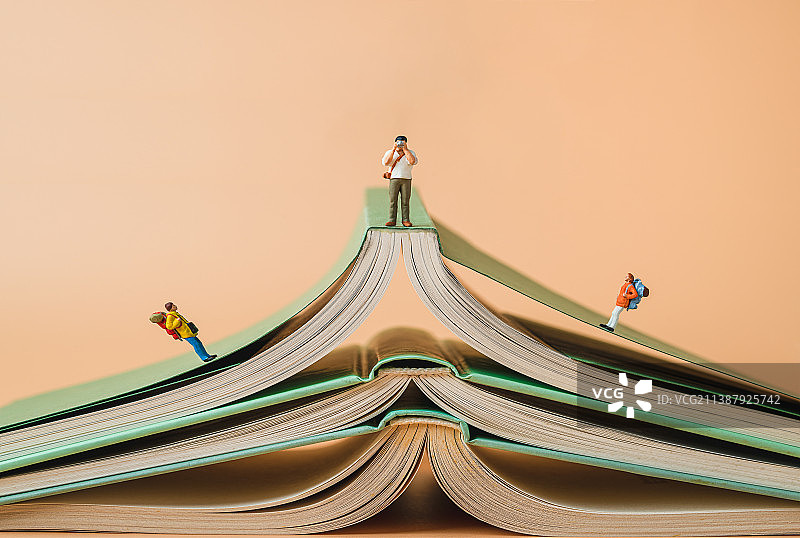 背包客在书籍的山峰上攀登远望拍照创意微缩景观图片素材