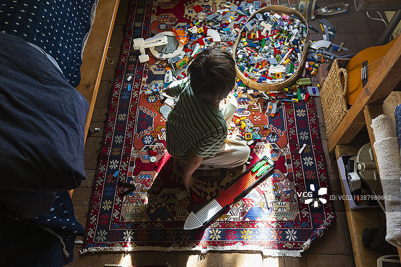 美国，男孩坐在阳光下的卧室地板上的玩具中图片素材