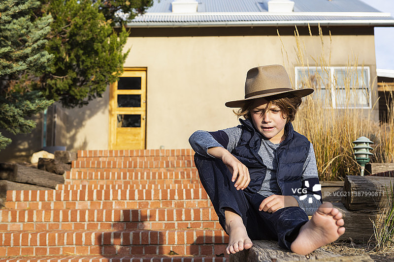 居家生活：美国，戴着软呢帽的男孩在门廊放松身心图片素材