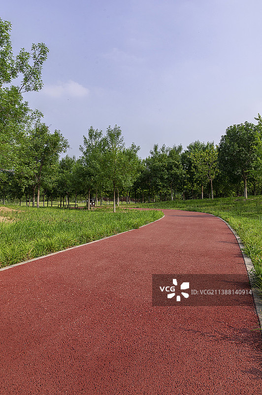 穿过公园绿色草地的红色健身塑胶跑道图片素材