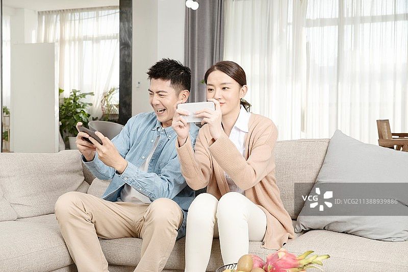 坐在沙发上互相玩手机游戏的年轻男女图片素材