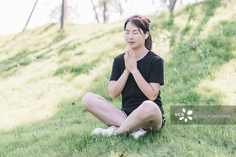 一位年轻亚洲女性在公园运动锻炼身体戴无线耳机练瑜伽图片素材