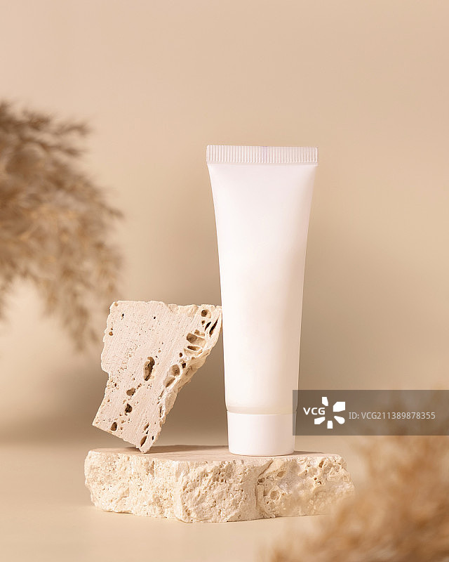 白色塑料乳霜软管在石头上，靠近浅黄色背景的干蒲苇草，模型图片素材