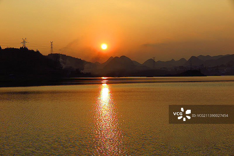 中国贵州贵阳清镇市红枫湖风光--夕阳下金色的湖面与湖岸d的山峦、村庄的炊烟、湖岸牧牛图图片素材