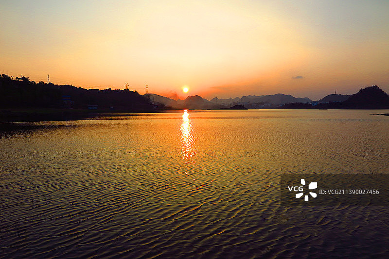 中国贵州贵阳清镇市红枫湖风光--夕阳下金色的湖面与湖岸d的山峦、村庄的炊烟、湖岸牧牛图图片素材
