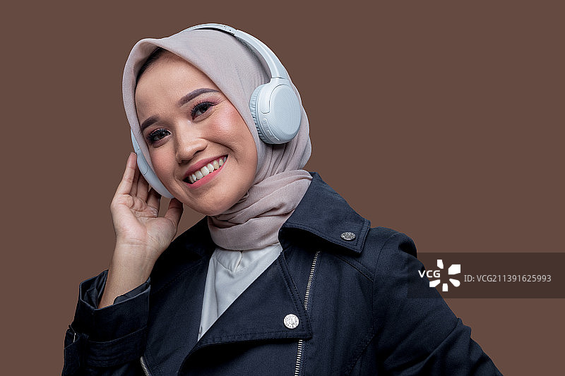 戴着无线耳机，面带微笑看着镜头的亚洲穆斯林女人图片素材